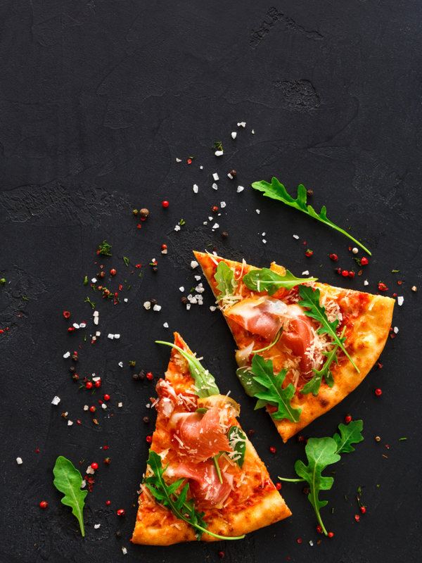 Slices of pizza with prosciutto and rocket salad with spices on black background
