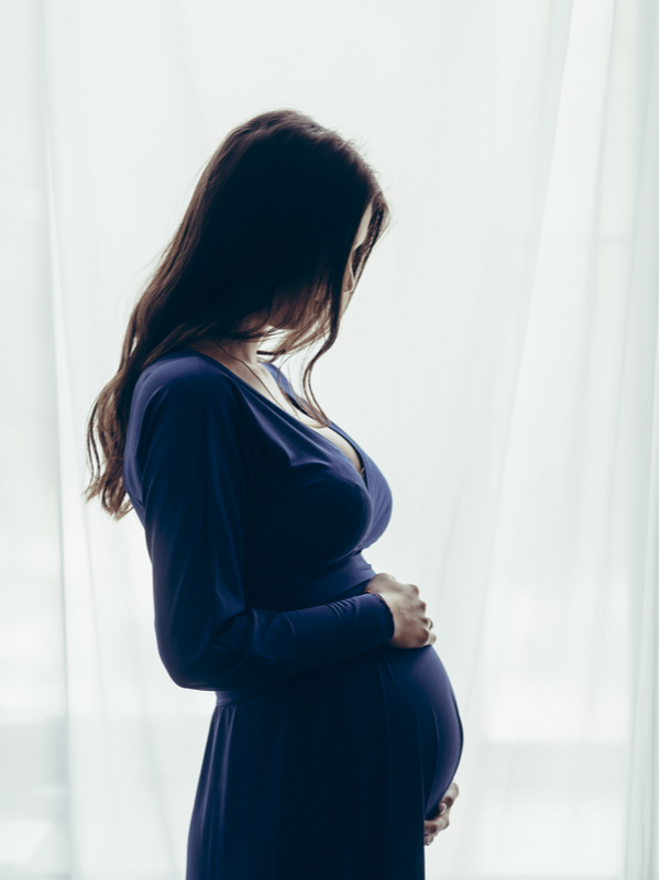 Pregnant woman in a blue dress at home standing against the window