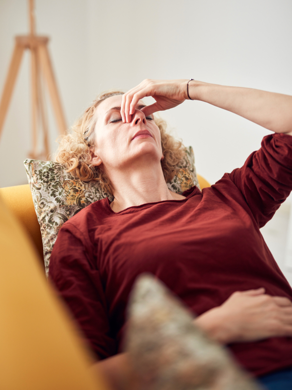Woman with headache, lying on a couch at home.