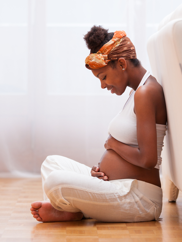 Young pregnant black woman seated on the floor touching her belly