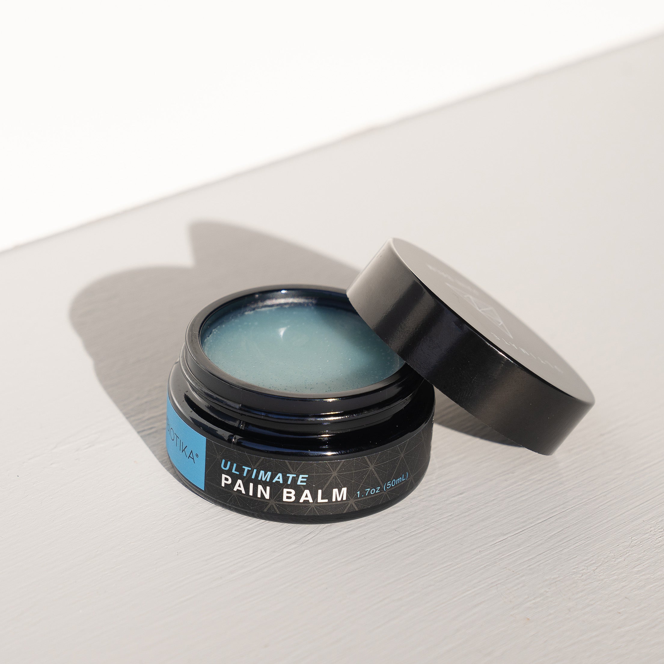 Ultimate Pain Balm Opened with Lid laying on Jar at an Angle