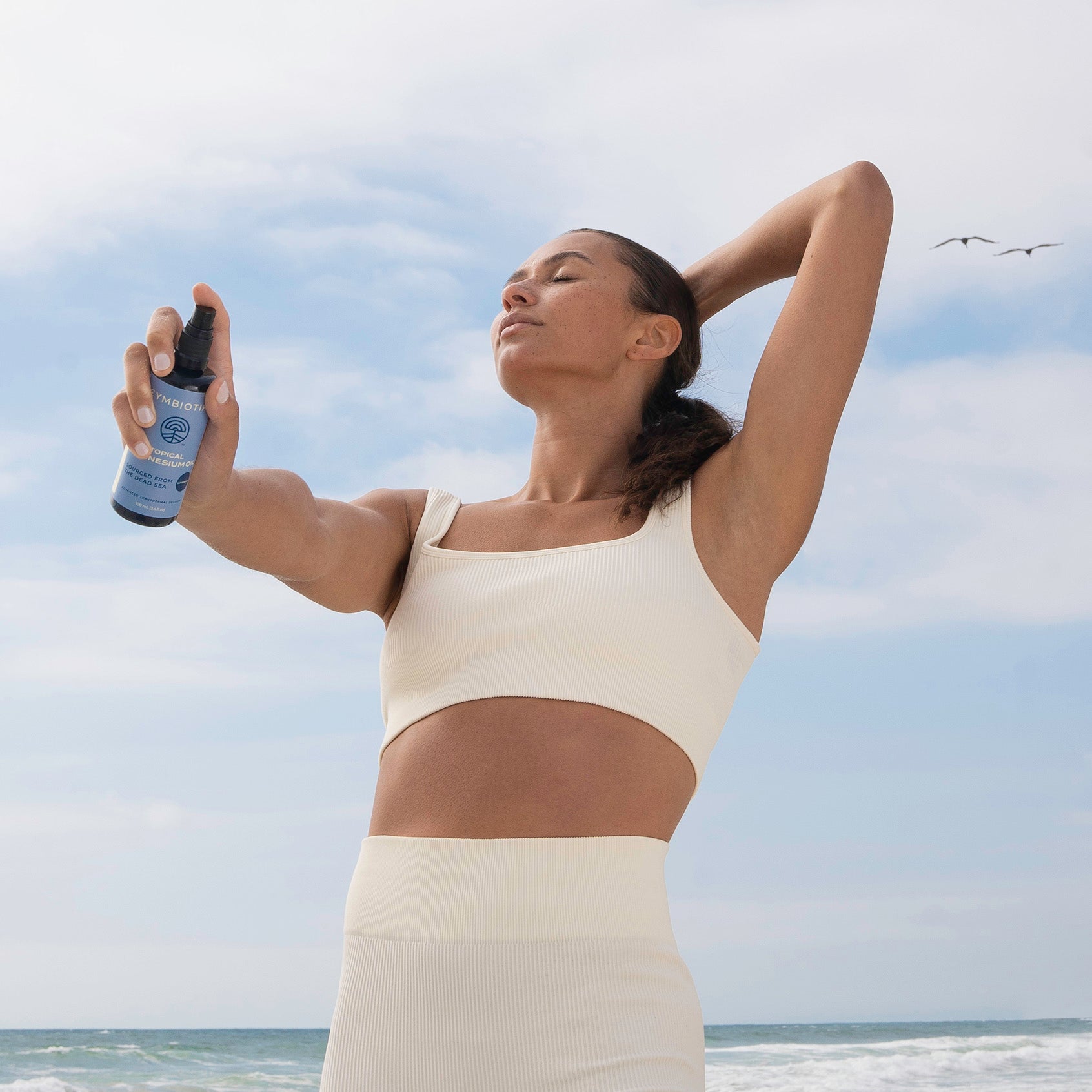Woman Holding Topical Magnesium Oil Spray Bottle on Beach